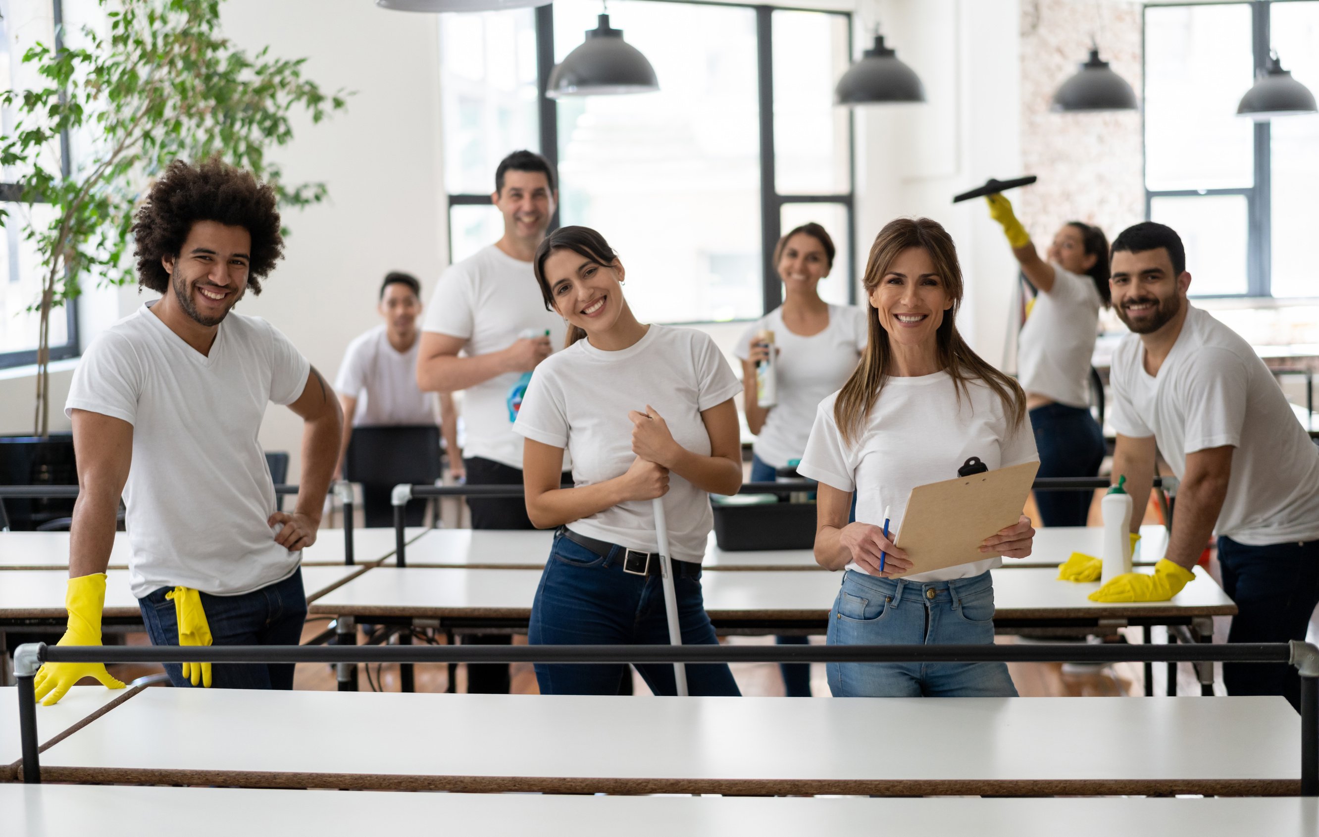 Friendly cleaning crew at an office all smiling at camera holding each cleaning supplies and equipment